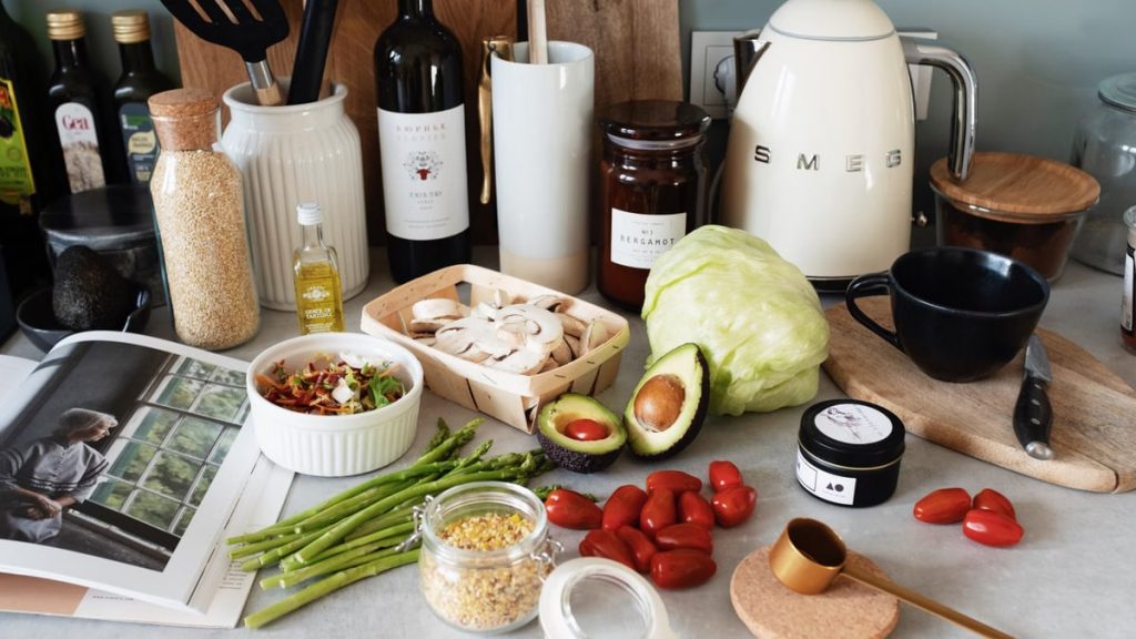 Assorted healthy food and vegetables set locating on gray countertop next to various utensils and appliances during cooking in stylish kitchen