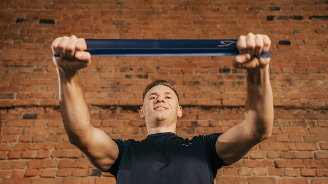 Man performing workout with resistance band against a brick wall backdrop.